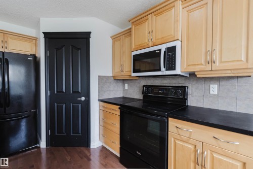Kitchen featuring wood cabinetry, black appliances, dark countertops, and tile backsplash - 1951 120 Street, Edmonton, AB - Indoor Photo Showing Kitchen