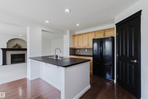 Kitchen with wood-finish flooring, an island featuring a stainless steel sink, black countertops, and light wood cabinetry - 1951 120 Street, Edmonton, AB - Indoor Photo Showing Kitchen