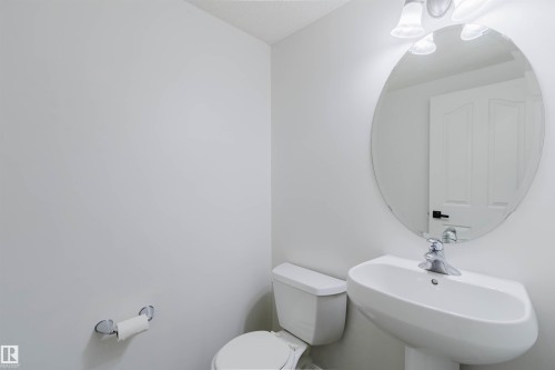 Pedestal sink with chrome faucet, oval mirror, and three-bulb vanity light fixture - 1951 120 Street, Edmonton, AB - Indoor Photo Showing Bathroom