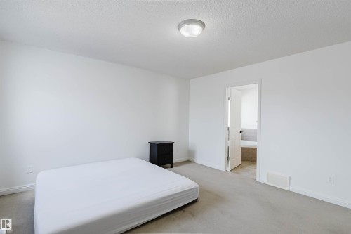 Spacious room featuring neutral carpeting, white painted walls, a flush-mount ceiling light, and a white interior door leading to a tiled bathroom - 1951 120 Street, Edmonton, AB - Indoor Photo Showing Bedroom