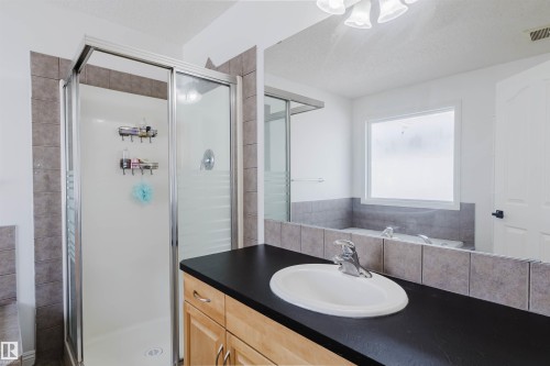 Bathroom featuring a glass-enclosed shower, a built-in tub with tile surround, a single vanity with a dark countertop and undermount sink, and light wood-finish cabinetry - 1951 120 Street, Edmonton, AB - Indoor Photo Showing Bathroom