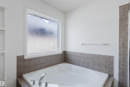 White soaking tub with deck-mounted chrome fixtures, set against neutral square wall tile - 1951 120 Street, Edmonton, AB - Indoor Photo Showing Bathroom