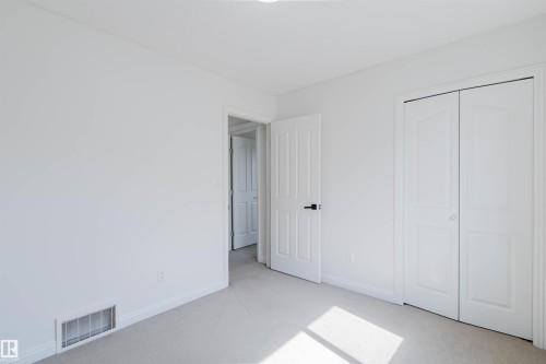 Carpeted room featuring a white interior door with black hardware, a bi-fold closet door, baseboard trim, and a floor vent - 1951 120 Street, Edmonton, AB - Indoor