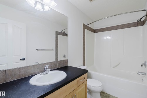 Bathroom featuring a wood-finish vanity with a dark countertop and integrated sink, a large wall-mounted mirror, a tiled backsplash, and a shower-over-tub combination with a curved shower rod - 1951 120 Street, Edmonton, AB - Indoor Photo Showing Bathroom