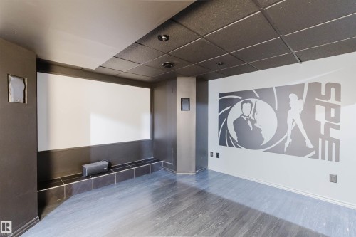 Dedicated media room featuring a large projection screen, recessed lighting, built-in wall speakers, dark acoustic ceiling tiles, and wood-finish flooring - 1951 120 Street, Edmonton, AB - Indoor Photo Showing Other Room
