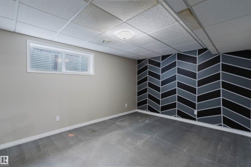 Room featuring a geometric accent wall, drop ceiling, and gray carpeting - 1951 120 Street, Edmonton, AB - Indoor