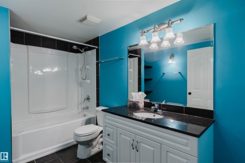 Bathroom with a white tub and shower combination, black tiled flooring, a white vanity with a dark countertop, a rectangular mirror, and a multi-bulb vanity light fixture - 1951 120 Street, Edmonton, AB - Indoor Photo Showing Bathroom