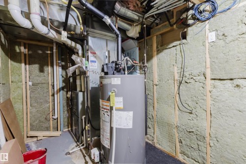Utility room featuring a water heater, furnace, exposed insulation, PVC piping, and electrical conduits - 1951 120 Street, Edmonton, AB - Indoor Photo Showing Basement