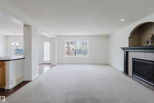Spacious living area featuring light-colored carpeting, a fireplace with a tiled surround and dark wood mantel, and large windows - 1951 120 Street, Edmonton, AB - Indoor Photo Showing Living Room With Fireplace