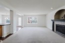 Spacious living area featuring light-colored carpeting, a fireplace with a tiled surround and dark wood mantel, and large windows - 1951 120 Street, Edmonton, AB  - Indoor Photo Showing Living Room With Fireplace 