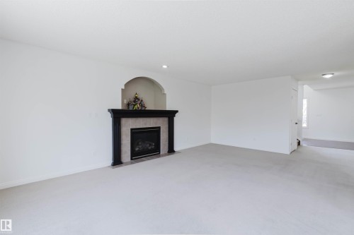 Living area featuring a fireplace with a dark wood mantel and a tiled surround, an arched alcove, recessed lighting, and neutral carpeting - 1951 120 Street, Edmonton, AB - Indoor Photo Showing Other Room With Fireplace