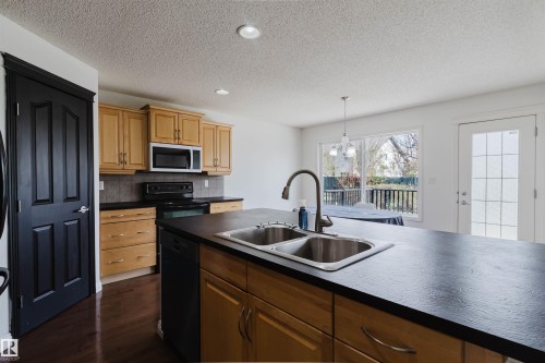 Kitchen featuring an island with a double basin sink and gooseneck faucet, light wood cabinetry, dark countertops, and stainless steel appliances - 1951 120 Street, Edmonton, AB - Indoor Photo Showing Kitchen With Double Sink