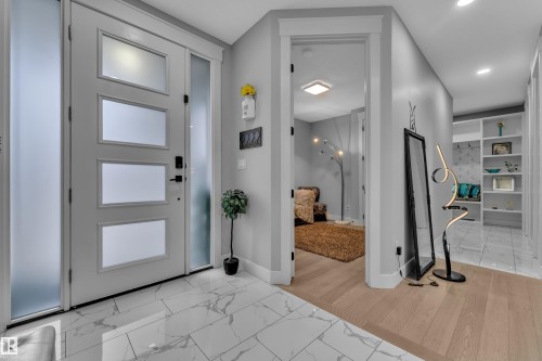Entryway featuring a contemporary front door with frosted glass panels and sidelights, large format marble-look tile flooring, light wood-finish flooring, recessed lighting, and built-in shelving - 8025 174A Avenue, Edmonton, AB - Indoor Photo Showing Other Room