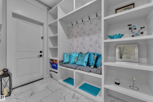 Entryway featuring built-in white shelving, integrated bench seating with storage, a white paneled door with black hardware, and patterned floor tile - 8025 174A Avenue, Edmonton, AB - Indoor With Storage