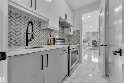 Galley kitchen featuring herringbone tile backsplash, white countertops, stainless steel appliances, and white and gray cabinetry - 8025 174A Avenue, Edmonton, AB - Indoor Photo Showing Kitchen With Upgraded Kitchen