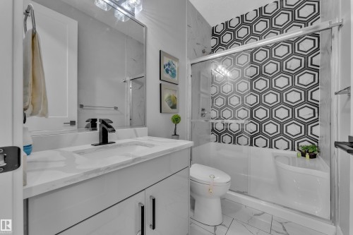 Contemporary bathroom featuring a black and white geometric tiled shower surround, a white vanity with an integrated sink, a black faucet, and coordinating black hardware - 8025 174A Avenue, Edmonton, AB - Indoor Photo Showing Bathroom