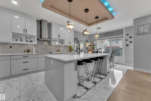 Modern kitchen featuring an expansive center island with seating, glossy white cabinetry, and a herringbone tile backsplash - 8025 174A Avenue, Edmonton, AB - Indoor Photo Showing Kitchen With Upgraded Kitchen