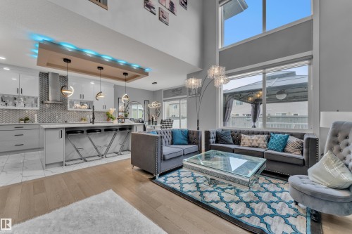 Contemporary open-concept living space featuring high ceilings, large windows, wood-finish flooring, a modern kitchen with a central island, and sleek cabinetry - 8025 174A Avenue, Edmonton, AB - Indoor Photo Showing Living Room