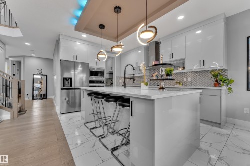 Contemporary kitchen featuring a large central island with seating, glossy white cabinetry, stainless steel appliances, and a herringbone-patterned tile backsplash - 8025 174A Avenue, Edmonton, AB - Indoor Photo Showing Kitchen With Upgraded Kitchen