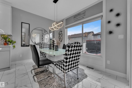 Dining area featuring a contemporary linear chandelier with an illuminated design, large picture window, and white marble-look tile flooring - 8025 174A Avenue, Edmonton, AB - 