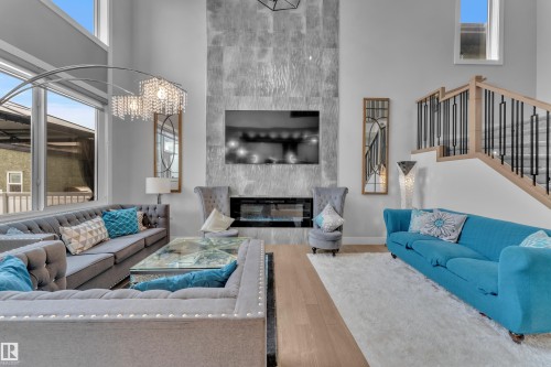 Two-story living area featuring a prominent fireplace with a textured surround, large window wall, and wood-finish flooring - 8025 174A Avenue, Edmonton, AB - Indoor Photo Showing Living Room With Fireplace