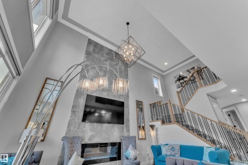 Two-story living area featuring a vaulted ceiling with crown molding, a built-in fireplace with a stone surround, and an open staircase with metal balusters and wood handrails - 8025 174A Avenue, Edmonton, AB - Indoor Photo Showing Other Room With Fireplace