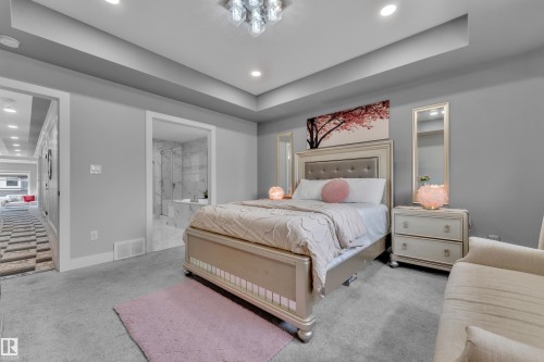 Carpeted bedroom featuring a tray ceiling with recessed lighting and a contemporary chandelier - 8025 174A Avenue, Edmonton, AB - Indoor Photo Showing Bedroom