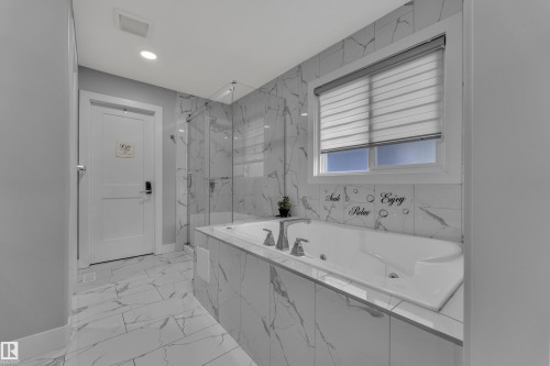 Bathroom featuring a built-in jetted tub, glass-enclosed shower, white marble-look tile flooring, white marble-look tile surround, and a window with horizontal blinds - 8025 174A Avenue, Edmonton, AB - Indoor Photo Showing Bathroom