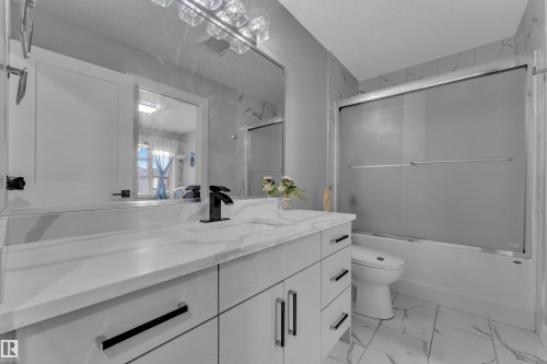Modern bathroom featuring a single vanity with a white countertop and integrated sink, matte black faucet, and white cabinetry with black hardware - 8025 174A Avenue, Edmonton, AB - Indoor Photo Showing Bathroom