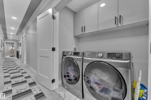 Dedicated laundry area featuring modern front-load appliances, overhead storage cabinetry, and a white tile flooring - 8025 174A Avenue, Edmonton, AB - Indoor Photo Showing Laundry Room