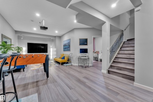Open-concept lower level featuring wood-finish flooring, recessed lighting, and a prominent staircase with metal balusters - 8025 174A Avenue, Edmonton, AB - Indoor Photo Showing Other Room