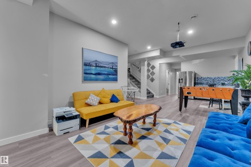 Open-concept recreation area featuring wood-finish flooring, recessed lighting, a ceiling-mounted projector, and a staircase with dark railings - 8025 174A Avenue, Edmonton, AB - Indoor