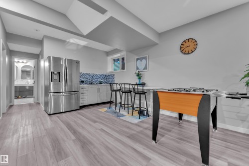 Recreation room featuring wood-finish flooring, a stainless steel refrigerator, a built-in wet bar with a blue tile backsplash, recessed lighting, and a window providing natural light - 8025 174A Avenue, Edmonton, AB - Indoor