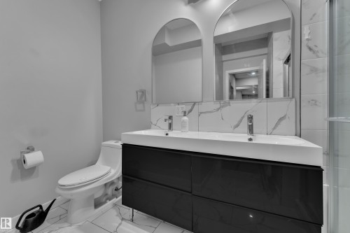 Contemporary bathroom featuring a double vanity with an integrated sink, two arched mirrors, white and gray veined tile backsplash, a matching tile floor, and a glass-enclosed shower - 8025 174A Avenue, Edmonton, AB - Indoor Photo Showing Bathroom