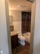 Full bathroom featuring a dark wood vanity with granite countertop, a built-in bathtub with shower, dark-toned tile surround, and coordinating floor tiles - 