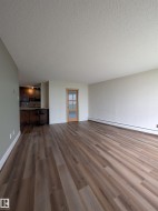 Spacious main living area featuring wood-finish flooring, light neutral wall colors, and a modern half-lite door - 