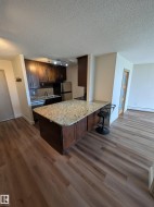 Kitchen featuring a granite countertop island with integrated cabinetry, stainless steel appliances, and wood-finish flooring - 