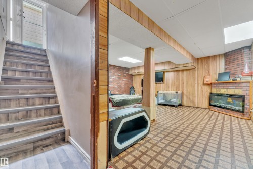 Finished lower level featuring a brick accent wall, a built-in fireplace with a hearth, wood-finish wall paneling, and a drop ceiling with recessed lighting - 4536 35A Avenue, Edmonton, AB - Indoor Photo Showing Other Room
