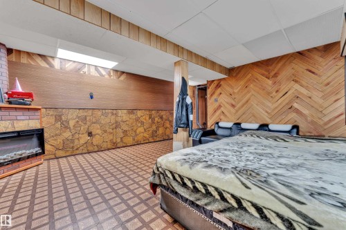 Spacious room featuring patterned floor tiles, a brick-surround fireplace with an electric insert, and a wood-paneled wall with a herringbone pattern - 4536 35A Avenue, Edmonton, AB - Indoor Photo Showing Other Room