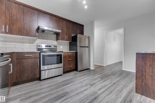 Kitchen featuring wood-finish cabinetry, stainless steel appliances, light-toned subway tile backsplash, and light wood-finish flooring - 2119 85 Street, Edmonton, AB - Indoor Photo Showing Kitchen