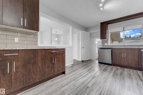 Kitchen featuring wood-finish cabinetry, light grey subway tile backsplash, light-toned countertops, stainless steel dishwasher, and wood-look flooring - 2119 85 Street, Edmonton, AB - Indoor Photo Showing Kitchen