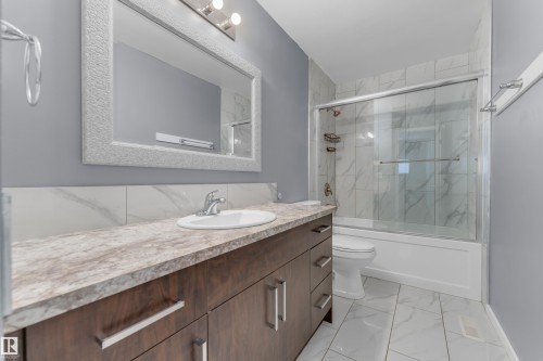Bathroom featuring a dark wood-finish vanity with a light-toned countertop, an undermount sink, and a framed mirror - 2119 85 Street, Edmonton, AB - Indoor Photo Showing Bathroom