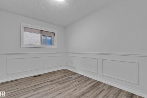 Interior room featuring wood-finish flooring, wainscoting, a window with white trim, and a ceiling-mounted light fixture - 2119 85 Street, Edmonton, AB - Indoor Photo Showing Other Room