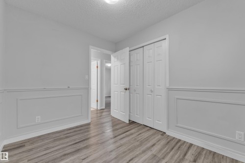 Interior room featuring wood-finish flooring, wainscoting, bi-fold closet doors, and light neutral wall tones - 2119 85 Street, Edmonton, AB - Indoor Photo Showing Other Room