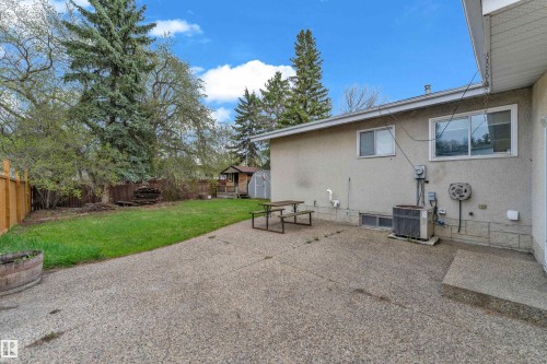 Spacious outdoor patio with exposed aggregate concrete, expansive lawn area, mature perimeter trees, and a wood privacy fence - 2119 85 Street, Edmonton, AB - Outdoor
