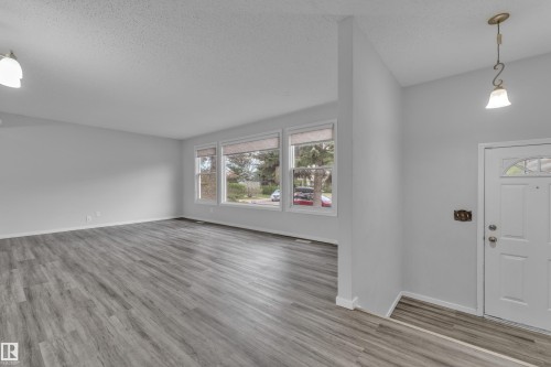 Spacious living area featuring wood-finish flooring, light grey wall paint, and multiple large windows - 2119 85 Street, Edmonton, AB - Indoor