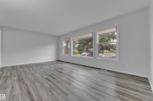Spacious room featuring neutral paint, wood-finish flooring, white baseboards, and three large windows with roller shades - 2119 85 Street, Edmonton, AB - Indoor Photo Showing Living Room