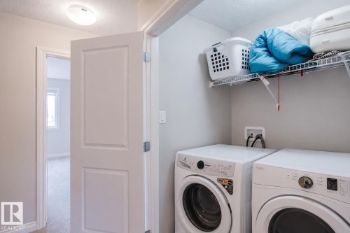 Dedicated laundry area featuring front-loading appliances, a wire storage shelf, and light gray wall paint - 328 West Haven Drive, Leduc, AB - Indoor Photo Showing Laundry Room