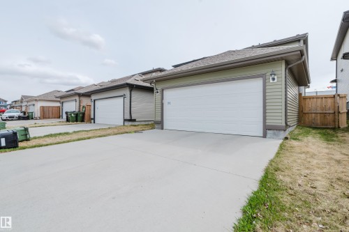 Light green siding exterior featuring a white garage door, concrete driveway, and asphalt shingle roof - 328 West Haven Drive, Leduc, AB - Outdoor