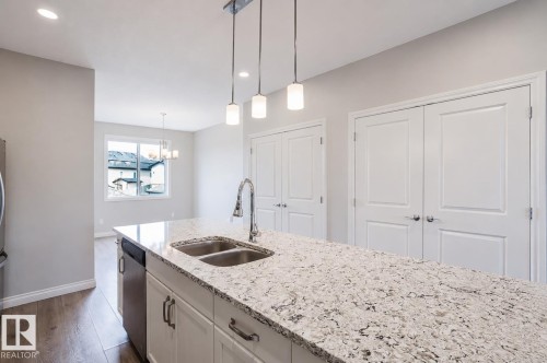 Kitchen island featuring a double basin stainless steel sink with a pull-down faucet, granite-style countertop, and white cabinetry with dark hardware - 328 West Haven Drive, Leduc, AB - Indoor Photo Showing Kitchen With Double Sink